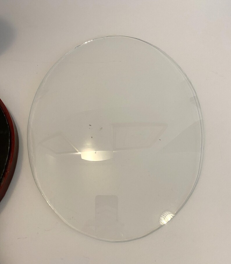 May include: A clear glass circle with a slightly chipped edge. The glass is smooth and reflective.