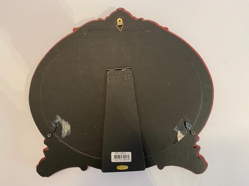 May include: A red ornate picture frame with a black backing and a gold hanging hook. The frame has a decorative design and a label on the back with the text "3621-03L* 92775 362183".