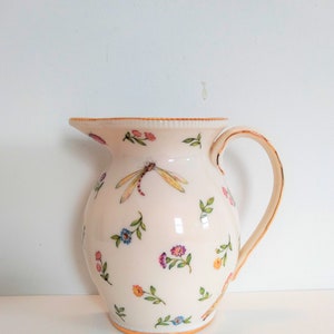 May include: A white ceramic jug with a gold rim and handle. The jug is decorated with a floral pattern and a dragonfly.