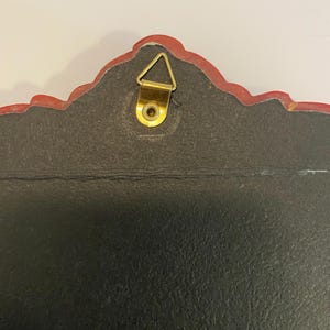 May include: The back of a red and gold framed wall hanging with a gold hanging hook.