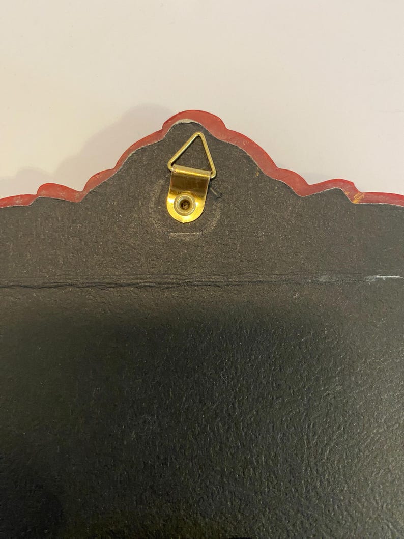 May include: The back of a red and gold framed wall hanging with a gold hanging hook.