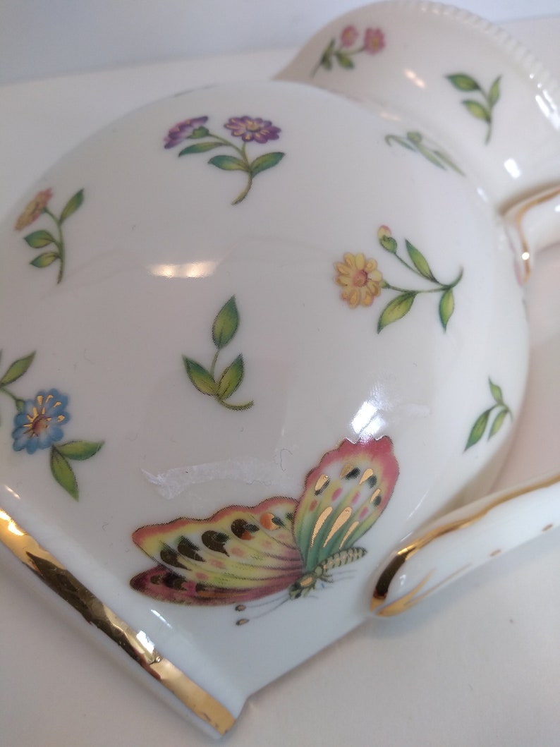 May include: White porcelain jug with a gold trim and a floral pattern. The jug features a butterfly with yellow, green, and pink wings.