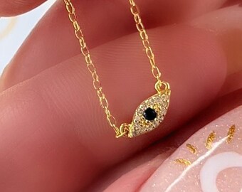 May include: A gold chain necklace with a small evil eye charm. The charm is set with white and black stones.