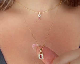 May include: Two gold necklaces with a key and padlock pendant. Both pendants are adorned with small white stones and a red stone in the centre.