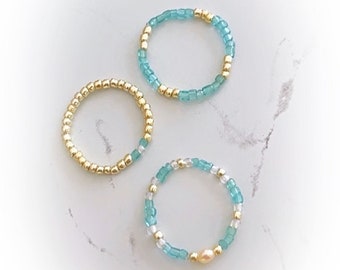 May include: Three beaded rings, one with a pearl accent. The rings are made with gold and turquoise beads.