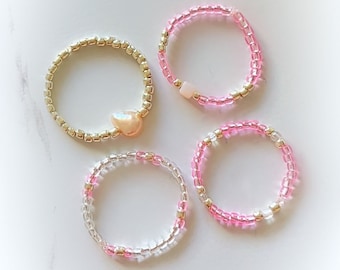 May include: Four beaded rings, two with pink beads and two with clear beads, one ring has a pearl accent.