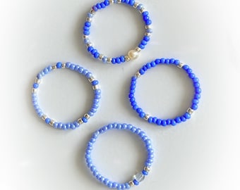 May include: Four beaded rings in shades of blue, with one ring featuring a pearl accent.
