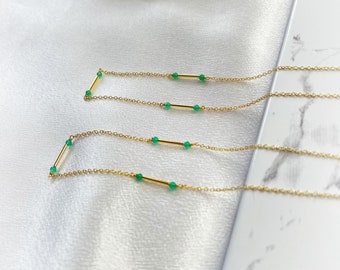 May include: Two gold necklaces with green gemstone beads and gold bar accents. The necklaces are layered on a white surface.
