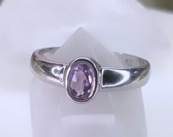 May include: A silver ring with a small, oval-shaped amethyst gemstone set in the centre.