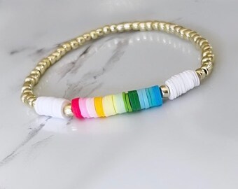 May include: A gold beaded bracelet with a rainbow of colourful beads. The beads are stacked in a row and are made of a smooth, round material.