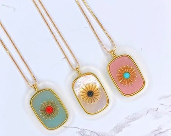 May include: Three gold necklaces with rectangular pendants featuring a stylised flower design. The pendants are made of different materials, including a light blue, a white, and a pink material. Each flower has a different coloured centre.