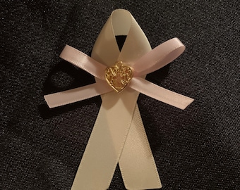 May include: A white satin ribbon tied into a bow with a gold heart charm featuring a cross design. The ribbon is on a black background.