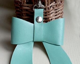 May include: A light blue leather bow keychain with a silver key ring and a silver button.