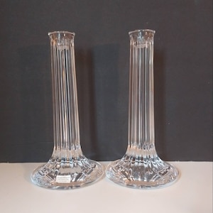 May include: Two clear glass candle holders with a fluted design. The candle holders are tall and slender with a wide base.
