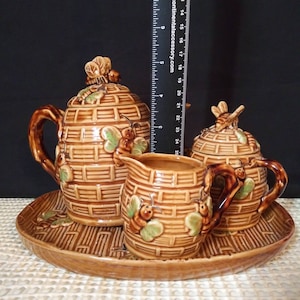 May include: A ceramic tea set with a beehive design. The set includes a teapot, creamer, sugar bowl, and a serving tray. The brown and tan set is decorated with bees and green leaves. The teapot measures approximately 9 inches tall.