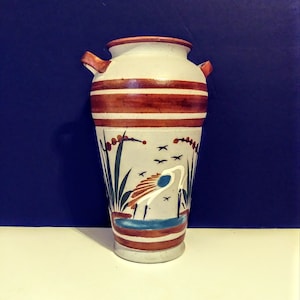 May include: A white ceramic vase with brown stripes and a painted design of a bird in a pond. The vase has two handles on the sides.