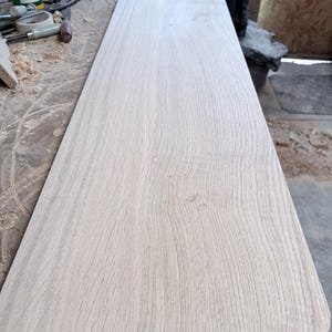 May include: A long, rectangular piece of light-coloured, unfinished wood board with a visible natural grain pattern. The board features smooth, flat surfaces and rounded corners on one end, showcasing the raw texture of the timber.