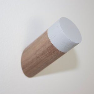 May include: A wooden wall hook with a white painted top. The hook is made of natural wood and has a simple, modern design.
