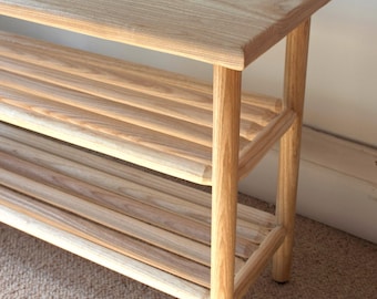 May include: A light wood shoe rack with two shelves and rounded legs. The rack is made of natural wood with a light grain pattern.