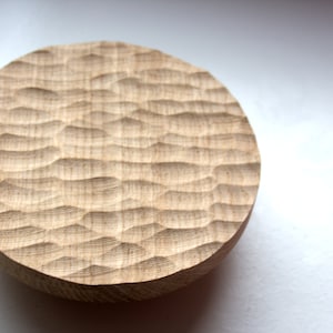 May include: A round wooden tray with a carved, wavy pattern. The tray is made of light brown wood and has a natural finish.