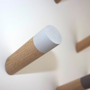 Könnte beinhalten: Ein Wandhaken aus Holz mit weiß lackierter Oberseite. Der Haken ist aus Naturholz gefertigt und hat ein schlichtes, modernes Design.