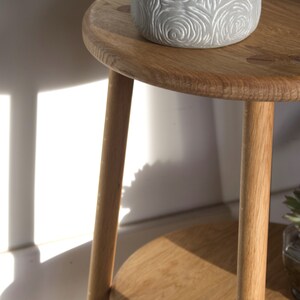 May include: A wooden plant stand with two shelves. The top shelf has a gray planter with a succulent plant. The stand has a natural wood finish.