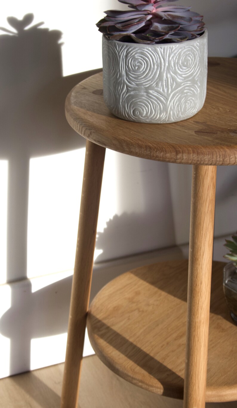 May include: A wooden plant stand with two shelves. The top shelf has a gray planter with a succulent plant. The stand has a natural wood finish.