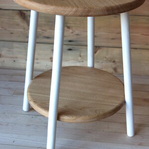 May include: A white painted wooden side table with a round top and a lower shelf. The table has four legs and is made of natural wood.