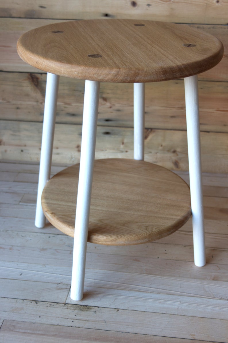 May include: A white painted wooden side table with a round top and a lower shelf. The table has four legs and is made of natural wood.