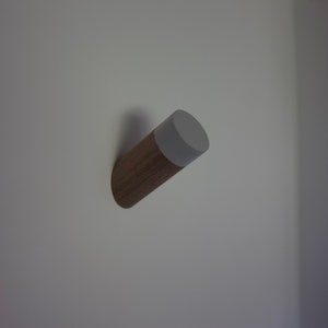 May include: A wooden wall hook with a gray painted top. The hook is mounted on a white wall.