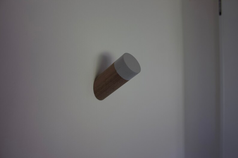 May include: A wooden wall hook with a gray painted top. The hook is mounted on a white wall.