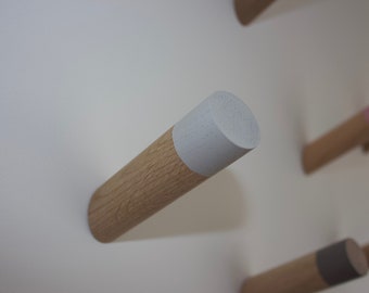 May include: A wooden wall hook with a white painted top. The hook is mounted on a white wall.