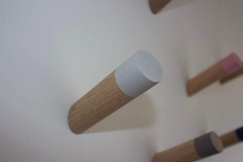 May include: A wooden wall hook with a white painted top. The hook is mounted on a white wall.