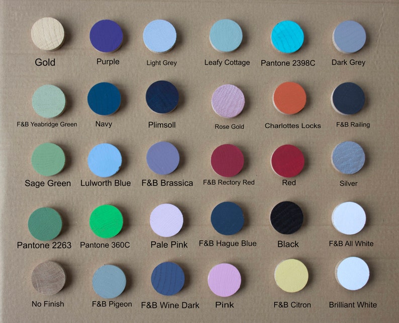 May include: A chart of 20 different paint colors, each color is represented by a small round wooden disc. The colors include gold, purple, light grey, leafy cottage, pantone 2398c, dark grey, f&b yeabridge green, navy, plimsoll, rose gold, charlottes locks, f&b railing, sage green, lulworth blue, f&b brassica, f&b rectory red, red, silver, pantone 2263, pantone 360c, pale pink, f&b hague blue, black, f&b all white, no finish, f&b pigeon, f&b wine dark, pink, f&b citron, and brilliant white.
