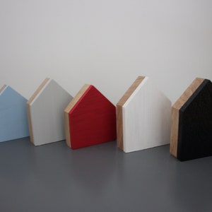May include: Five wooden house-shaped ornaments in different colors. The houses are arranged in a row from left to right: light blue, white, red, white, and black.