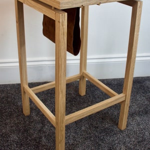 May include: A wooden side table with a leather strap hanging from the top. The table has a simple design with a square top and four legs.