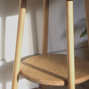 May include: A light wood side table with a round top and a lower shelf. The table has four legs that are turned and tapered.