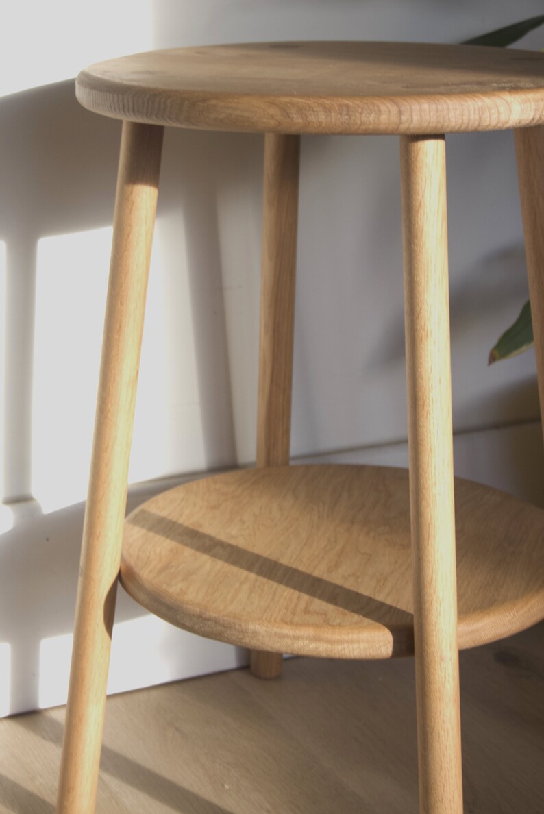 May include: A light wood side table with a round top and a lower shelf. The table has four legs that are turned and tapered.