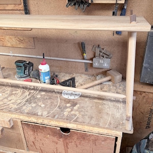 May include: A light-colored wooden console table featuring a rectangular top surface, four cylindrical legs, and a horizontal support bar connecting the legs. The table is constructed with visible joinery where the legs meet the tabletop surface.