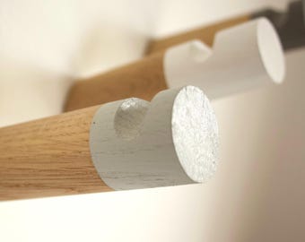 May include: Close-up of a wooden wall-mounted coat rack with white painted ends. The rack is made of natural wood with a light brown finish. The white painted ends are rounded and have a smooth finish.