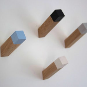 May include: Four wooden wall hooks with different colored square tops. The hooks are light brown wood with a light blue, white, gray, and black square on top.