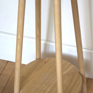 May include: A light wood side table with a round top and a lower shelf. The table has three legs and is made of natural wood.