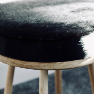 May include: A round stool with a natural wood frame and three legs. The seat is covered in black and white faux fur. The stool is a decorative piece of furniture.