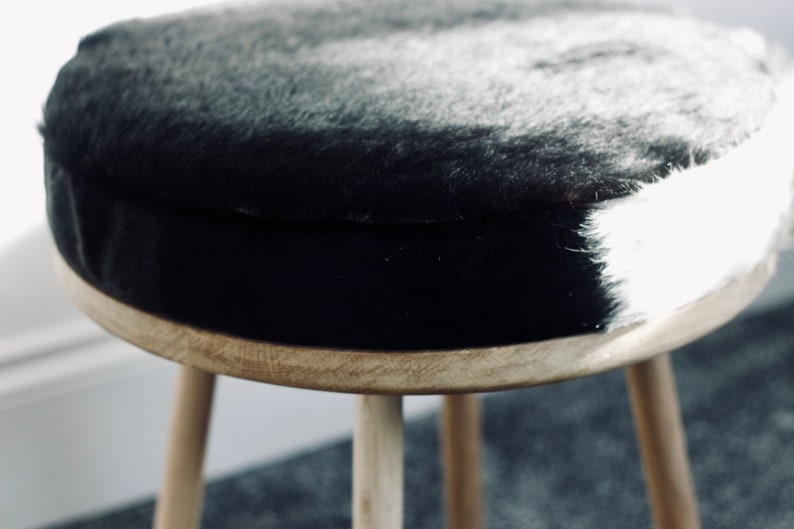 May include: A round stool with a natural wood frame and three legs. The seat is covered in black and white faux fur. The stool is a decorative piece of furniture.