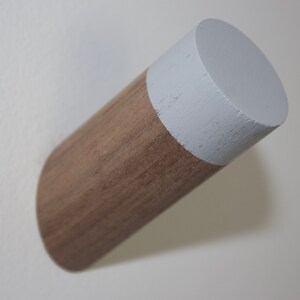 May include: A wooden wall hook with a white painted top. The hook is a cylinder shape and is mounted on a white wall.