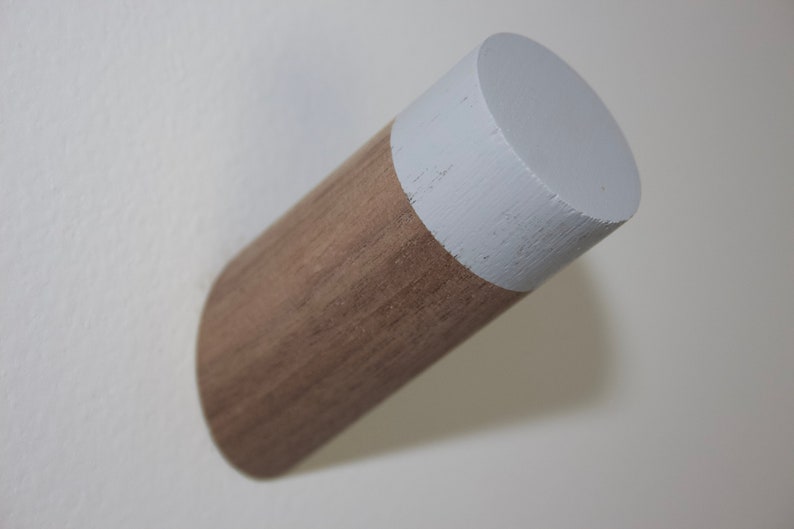 May include: A wooden wall hook with a white painted top. The hook is a cylinder shape and is mounted on a white wall.