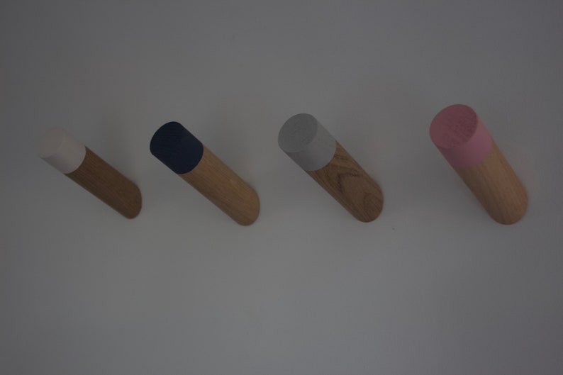 May include: Four wooden wall hooks with different colored tops. The hooks are white, navy blue, light gray, and pink.