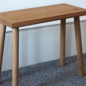 Handmade solid oak milking stool with four turned straight legs secured into position with contrasting wedged tenons finished in danish oil