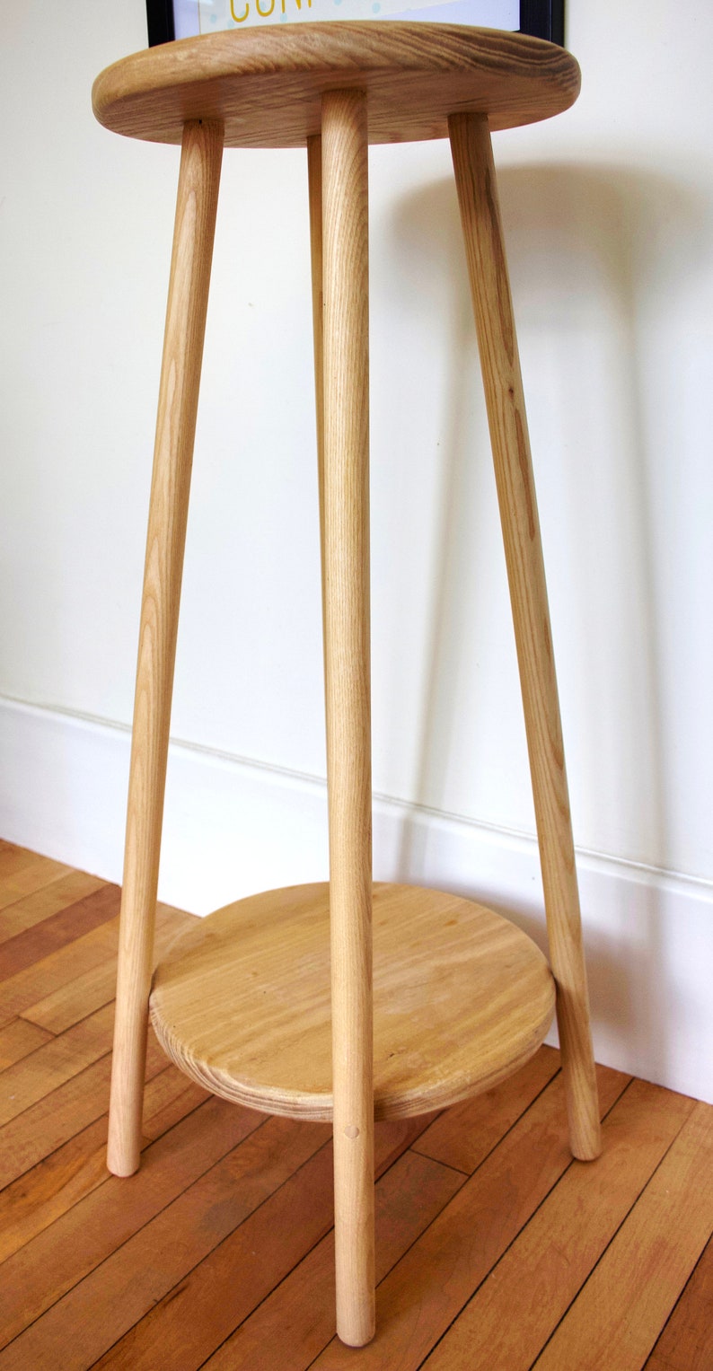 May include: A wooden side table with a round top and three legs. The table has a lower shelf.