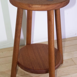 May include: A wooden stool with a round top and a lower shelf. The stool is made of dark brown wood and has three legs.
